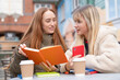 © Iryna - Friends share ideas while reading books at a cafe on a sunny day in the city