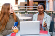© Iryna - Two women discuss ideas at a table outside a cafe during daytime in an urban setting