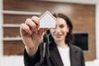 © wedmoments.stock - Female realtor holding house-shaped keychain with keys in front of a modern office interior, showcasing a welcoming atmosphere for potential home buyers and clients