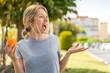 © luismolinero - Young blonde woman holding an orange at outdoors with surprise facial expression