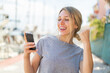 © luismolinero - Young blonde woman using mobile phone at outdoors celebrating a victory