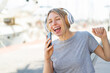 © luismolinero - Young blonde woman at outdoors listening music with a mobile and singing