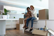 © wavebreak3 - Diverse couple on kitchen countertop unpacking moving boxes with smartphone, plant and lamp