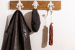 © David_Dietz - Eine geräucherte und getrocknete Wurst hängt neben einer Jacke und einer Mütze an einer Garderobe