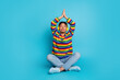 © deagreez - Young woman in colorful striped sweater meditating with headphones against blue background promoting style relaxation wellness fitness fashion