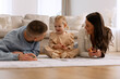 © Home-stock - Loving parents chatting with their cute daughter while drawing together, lying on floor carpet in living room