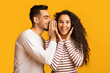 © Prostock-studio - Big Secret. Young Arab Man Sharing News With His Excited Girlfriend, Surprised Middle Eastern Woman Raising Hands In Amazement While Standing Together Over Yellow Studio Background, Free Space