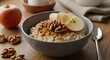 © firmanarif - A bowl of oatmeal with sliced apples and walnuts on a wooden table top, viewed from the side.