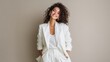© mila103 - Smiling young hispanic woman in white suit with curly hair against beige background.