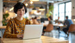 © AivaVisions - Young woman working on laptop in modern coworking space, confident freelance professional.