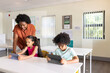 © Wavebreak Media - African American teacher leaning over girl and boy kids using tablets at white desks with posters