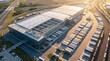 © SYATRI RAWU - Aerial drone view of a large logistics warehouse and distribution center with many trucks parked outside under a bright sun