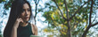 © aFotostock - Banner asian woman sitting green garden park using phone listen music from smart phone with laptop computer. Panorama Happiness Woman toothy smile laughing happy working on laptop with copy space