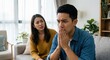 © Gayan - Unhappy Southeast Asian couple having relationship problems at home, stressed young man and woman sitting on sofa after argument in modern living room, concept of conflict and divorce.