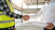 © Gayan - Close up of a multiethnic male engineer in a yellow safety vest shaking hands with an adult architect holding blueprints in a bright modern building construction site, business agreement concept