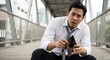 © Gayan - Distressed Southeast Asian businessman in white shirt sitting outdoors on an urban walkway looking at his empty wallet, feeling anxious about financial crisis and unemployment.