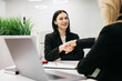 © wedmoments.stock - Young woman in black blazer is shaking hands with another professional in a modern office setting with a laptop and greenery visible on the desk during a business meeting