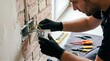 © Margarita Ratatosk - Electrician installing electrical outlet with wires in brick wall. Man worker connecting power for home renovation and construction.