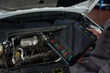 © pressmaster - Unknown man holding diagnostic tablet displaying engine performance data while standing in front of open car hood, analyzing vehicle condition in automotive workshop