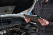 © pressmaster - Midsection of man holding digital tablet inspecting car engine in auto repair shop, standing near open hood, wearing work uniform, focusing on diagnostic process