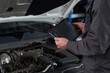 © pressmaster - Anonymous man using diagnostic tablet while inspecting car engine compartment, holding electronic device with graphs and data, focusing on automotive maintenance task