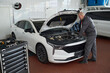 © pressmaster - Middle aged Caucasian man inspecting engine compartment of modern sedan in auto repair shop, standing beside open hood and focusing on car maintenance task, professional tools visible nearby