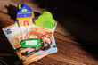 © Shutterly - Wooden toy house and keys on Euro currency bills on a dark table with sunlight for European housing market crisis and real estate problem.