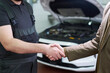 © pressmaster - Man in work overalls shaking hands with client in suit in front of car with open hood in auto repair shop, confirming agreement