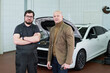© pressmaster - Caucasian middle aged man in suit standing next to Caucasian young adult man in mechanic uniform with arms crossed, both posing in front of car with open hood in auto repair shop