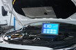 © pressmaster - Open car hood showing laptop with car service control panel interface resting on engine compartment, illustrating use of diagnostic technology in automotive maintenance setting