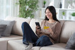 © Antonioguillem - Happy asian woman paying online sitting at home