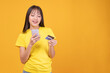 © kaew6566 - Happy young Asian woman using smartphone and holding credit card for online shopping. Beautiful female making mobile payment transaction on yellow background copy space. E-commerce fintech concept.