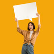 © Prostock-studio - Comment. Joyful caucasian lady having idea or thought, holding blank speech bubble cloud above her head, demonstrating free place for your text over yellow background