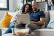 © nenetus - Happy beautiful couple using computer while sitting on the couch at home.