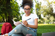 © Prostock-studio - Happy African American Student Girl Learning Using Laptop And Writing Taking Notes Wearing Earbuds Sitting In Park Outdoor. Studentship Leisure And Lifestyle. Online Education Concept
