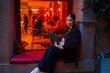 © BullRun - Hispanic middle aged woman seated on window ledge using tablet, calmly focused, showing connection with technology in personal space, illuminated by cozy indoor lighting.