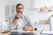 © Prostock-studio - Thoughtful middle aged caucasian man student with beard in glasses works at laptop and watch online lesson in minimalist kitchen interior. Brainstorm, creative idea for remote work, study due covid-19