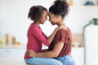 © Prostock-studio - Profile portrait of happy black mother and daughter hugging and smiling at each other, beautiful young african american woman mom and teen girl kid cuddling at kitchen, copy space, side view
