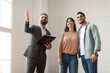 © Prostock-studio - Portrait Of Male Realtor Or Architect Wearing Suit Showing New Empty House To Smiling Millennial Buyers, Pointing. Husband Embracing His Wife, Visiting Residential Building, Choosing Home For Family