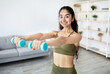 © Prostock-studio - Home training concept. Active Indian lady working out with dumbbells indoors. Sporty Eastern woman exercising her biceps muscles, doing domestic sports during covid pandemic