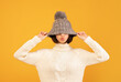 © Prostock-studio - Pretty young woman pulling down woollen hat, showing kissing lips, fooling and posing to camera over yellow background. Happy lady in fashionable winter outfit being silly
