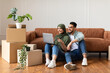 © Prostock-studio - Young Muslim Couple Using Laptop Sitting On Floor After Moving New Home. Real Estate, House Ownership And Relocation Concept. Spouses Browsing Internet Sitting Among Carton Boxes, Pointing At Screen