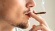 © Haven - Person outdoors holding lit cigarette with smoke rising, set against blurred green and yellow natural background.