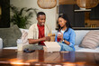 © wavebreak3 - African American couple sharing takeout on sofa in living room with takeout boxes and clear cups