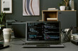 © AnnaStills - Laptop displaying programming code on screen positioned on office desk with takeaway coffee cups, smartphone, and stationery in modern workspace, no people visible