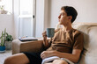 © kleberpicui - Teenage boy sitting on a sofa at home holding a cup of hot drink. Cozy lifestyle, comfort, rest, study break and quiet moment indoors
