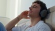 © Yuliia - Relaxed Caucasian man in bedroom at home wearing headphones enjoying music sound calm male guy relax closed eyes listening song playlist audio gadget technology wireless earphones satisfaction indoors