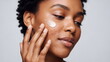 © xuxu - Woman applying cream on her face with acne problem. Skincare routine and beauty treatment. Dermatology and skin health care. Gray background.