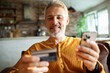 © Geber86 - Smiling middle aged man making mobile payment at home