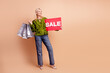 © deagreez - Senior shopper woman with sale sign and shopping bags smiles in fashionable beige background casual glamour